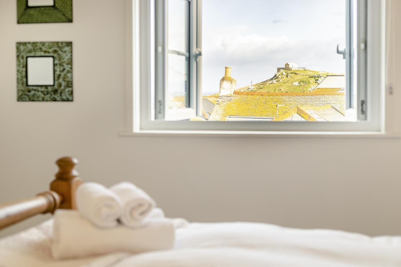 A hotel room with a bed, a window with a view of a building, and a wall with two framed pictures.
