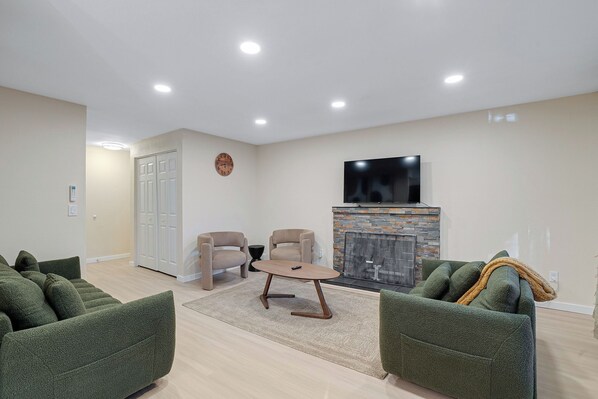Una sala de estar moderna con chimenea, dos sillones, un sofá y un televisor sobre la chimenea.