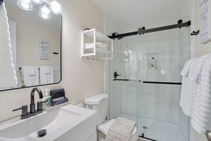 Un baño con lavamanos blanco, un espejo con iluminación, cabina de ducha de vidrio y un perchero para toallas.