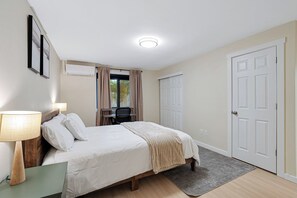 Un dormitorio con cama, mesita de noche, lámpara, ventana con cortinas, escritorio, silla y armario.