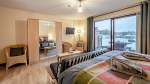 A hotel room with a bed, a seating area with chairs, a TV, and a view of a water body. - 4 Bed in Horning (oc-s34101) (Horning)