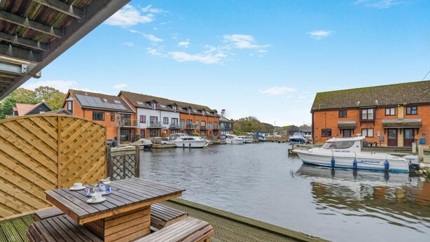 A riverside view with wooden dock, boats, and traditional buildings. - 4 Bed in Horning (oc-s34101) (Horning)