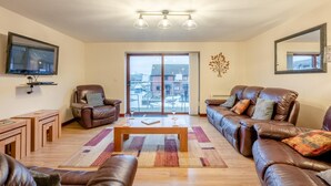 A living room with a sofa, armchair, coffee table, and a TV mounted on the wall. - 4 Bed in Horning (oc-s34101) (Horning)