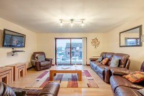 Ein Wohnzimmer mit Sofa, Sesseln, Couchtisch und einem an der Wand befestigten Fernseher.