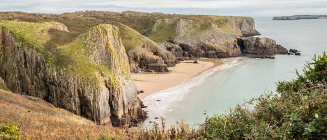 A coastal landscape with rocky cliffs, a sandy beach, and a calm sea.