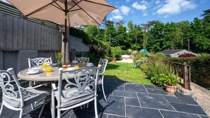 Une terrasse extérieure avec une table et des chaises, un grand parasol et un jardin en arrière-plan.