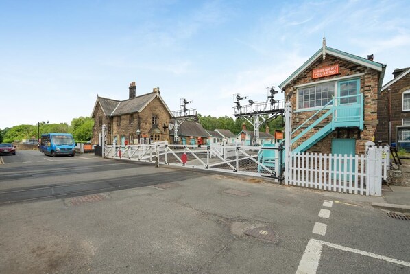 A railway crossing with a blue train, a white fence, and a building with a sign that reads 'Grosmont Crossing'. - 3 Bed in Grosmont (oc-wa060) (Grosmont)