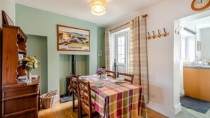 Un coin repas avec une table dressée pour quatre personnes, un buffet en bois, un tableau encadré et une fenêtre avec des rideaux.