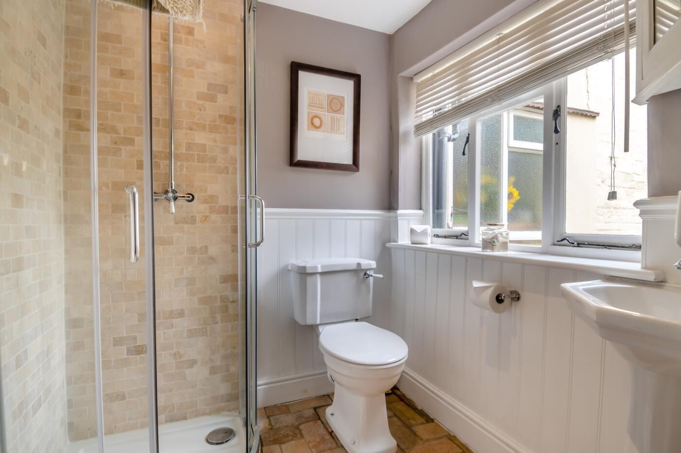 Une salle de bain avec une douche à parois de verre, des toilettes, un lavabo et une fenêtre avec des stores.