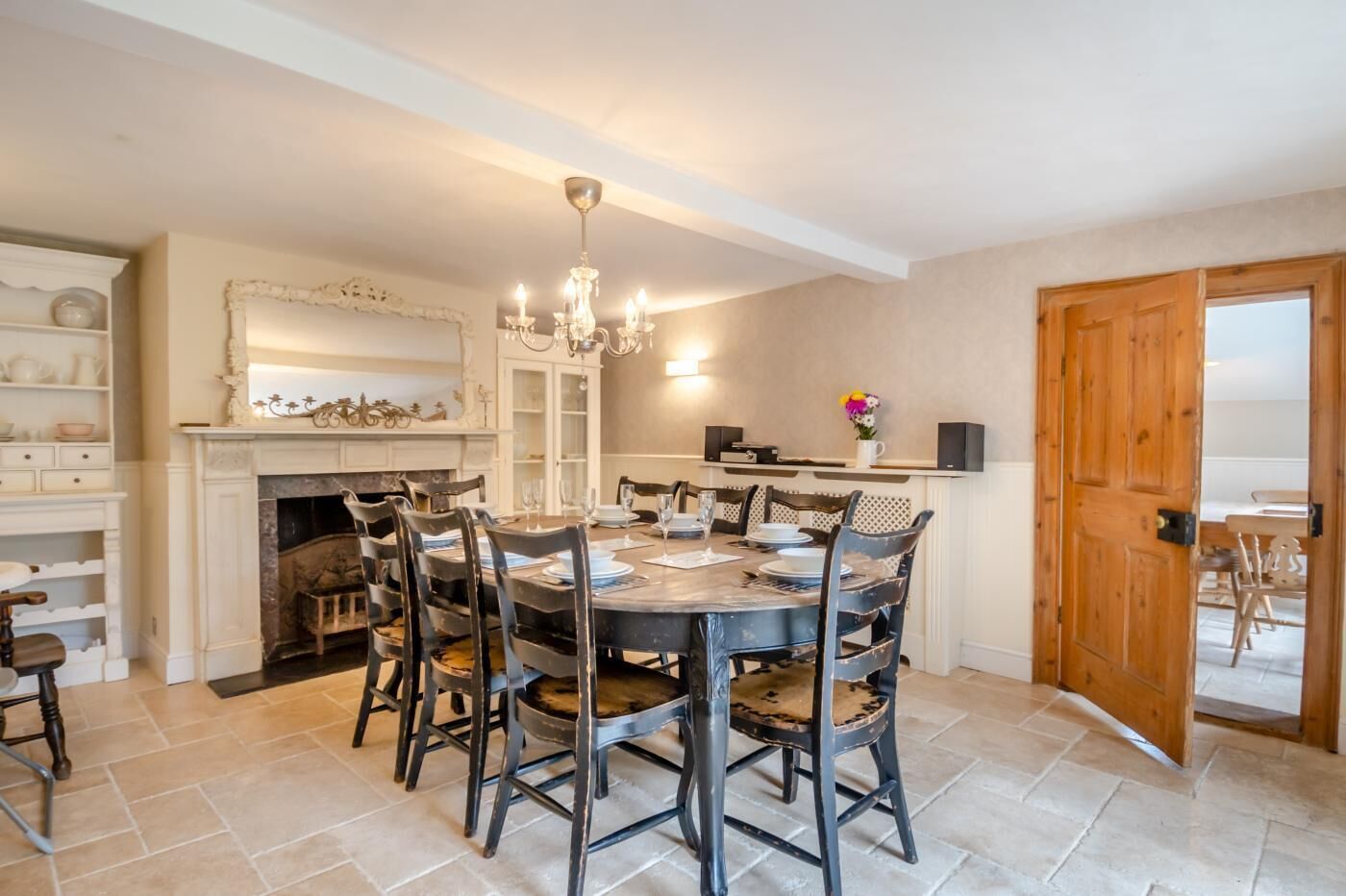 Un coin repas comprenant une table ronde, six chaises, un lustre, une cheminée et une porte en bois.