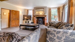 Ein gemütliches Wohnzimmer mit Kamin, Fernseher und gemusterten Sofas.