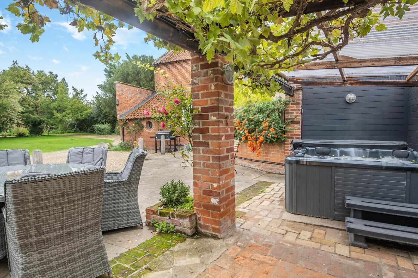 A patio area with wicker furniture, a brick wall, and a hot tub.