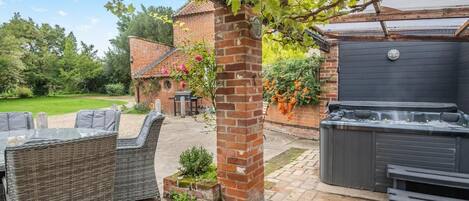 A patio area with wicker furniture, a brick wall, and a hot tub.