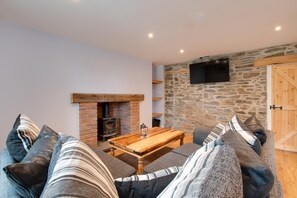 Un salon chaleureux avec un mur en pierre, une cheminée, une table en bois et un canapé agrémenté de coussins à rayures.