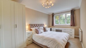 Une chambre à coucher comprenant un lit, des tables de chevet, une commode, une fenêtre avec des rideaux et un luminaire au plafond.