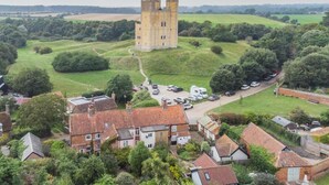 Une tour historique, entourée d’une végétation luxuriante, et un petit village aux maisons traditionnelles.