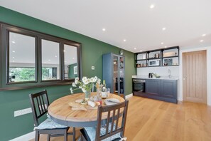 A modern kitchen with dark cabinets, a built-in microwave, and a wooden dining table with chairs. - 5 Bed in Woolacombe (oc-alba12) (Woolacombe)