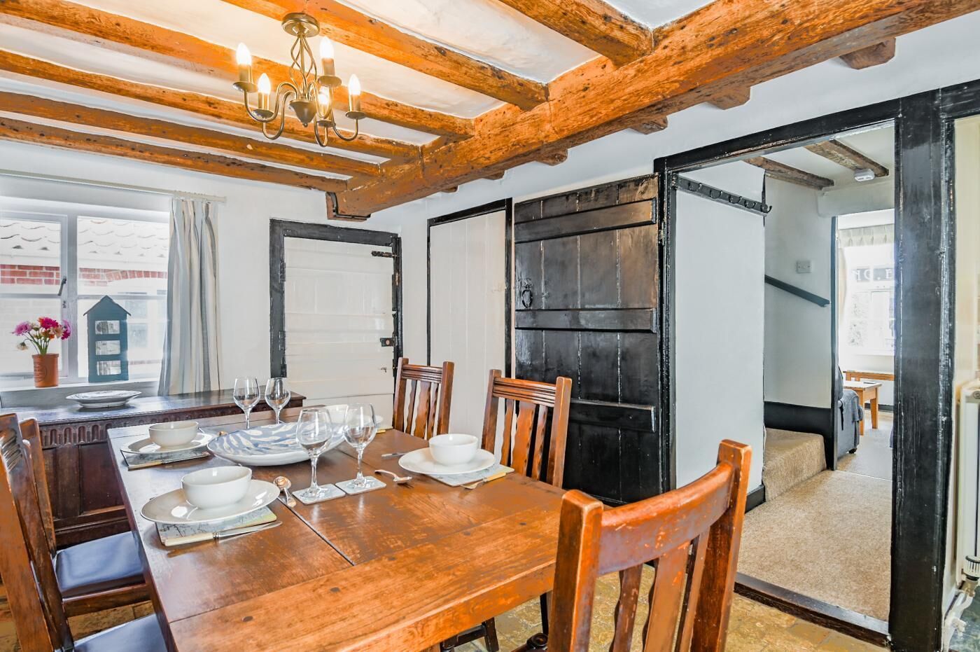 A dining area with a wooden table set for four, a chandelier, and a view through an open door.