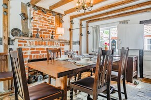 Un coin repas rustique avec un mur en briques, des poutres en bois et une table dressée pour quatre personnes.