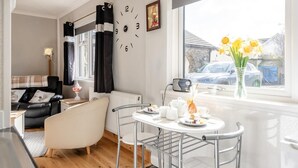 A modern living room with a dining area, a radiator, a clock, and a window with a view of the outside. - 1 Bed in Stepaside (oc-pw9268) (Amroth)