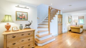 A staircase with wooden steps and a white railing, a wooden dresser with drawers, a lamp, a framed painting, and a sofa in a room with wooden flooring. - 3 Bed in Ufford (oc-sfmea) (Ufford)