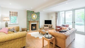 A living room with a fireplace, sofa, television, and large windows. - 3 Bed in Ufford (oc-sfmea) (Ufford)
