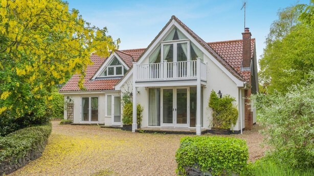 A two-story house with a balcony, a chimney, and a gravel driveway. - 3 Bed in Ufford (oc-sfmea) (Ufford)