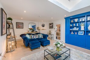 Een moderne woonkamer met een blauwe bank, een glazen salontafel en een blauwe wandplank.