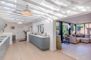 Een moderne keuken met een centraal eiland, een zithoek met een bank, en uitzicht op de tuin door grote ramen.
