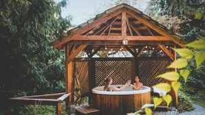 A wooden gazebo with a hot tub, surrounded by greenery.