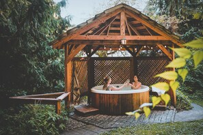 Un pabellón de madera con un jacuzzi, rodeado de follaje.