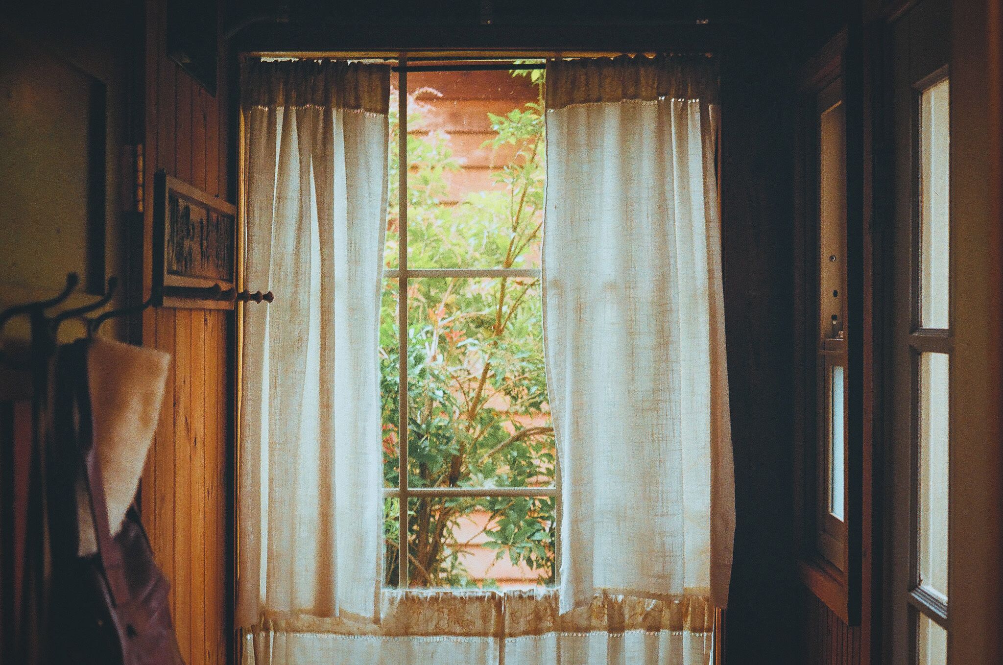 A room with a window covered by curtains, a wooden door, and a towel hanging on a rack.