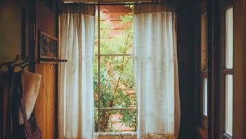 A room with a window covered by curtains, a wooden door, and a towel hanging on a rack.