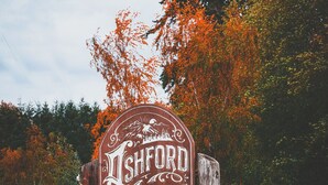 Een houten bord met de tekst 'Fishord Lodge', omringd door herfstbladeren.
