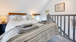 Een slaapkamer met een groot bed, twee nachtkastjes, een houten hoofdbord, een grijze leuning en een ingelijste foto aan de muur.