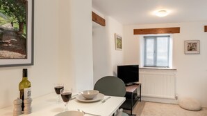 Een eetgedeelte met een tafel gedekt voor twee personen, een televisie en een raam met jaloezieën.