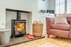A modern living room with a wood-burning stove, a wicker basket, and a sofa with patterned cushions. - 2 Bed in Orford (oc-sfcto) (Orford)