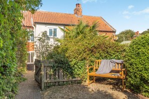 A garden with a wooden bench, a brick house with a tiled roof, and a wooden fence. - 2 Bed in Orford (oc-sfcto) (Orford)