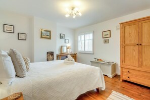 Ein Schlafzimmer mit einem großen Bett, einem Holzschrank, einem Schreibtisch mit Lampe sowie gerahmten Bildern an den Wänden.
