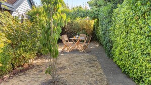 Une terrasse de jardin avec une table et des chaises, entourée d’une végétation luxuriante et avec une maison en arrière-plan.