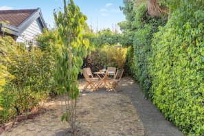Eine Gartenpatio mit Tisch und Stühlen, umgeben von üppiger Vegetation und einem Haus im Hintergrund.