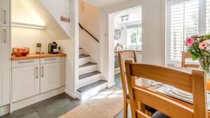 Une cuisine avec des meubles blancs, un plan de travail en bois et un coin repas comprenant une chaise et une table en bois.