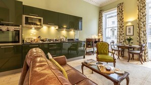 A modern kitchen with dark green cabinets, a dining area with a green armchair, and a leather sofa. - 1 Bed in Bath (oc-bhr5) (Bath)