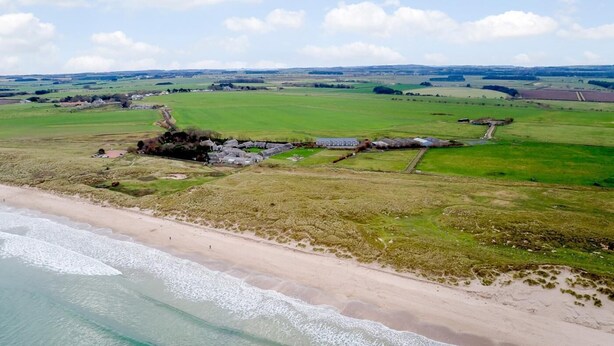 An aerial view of a coastal area with a sandy beach, green fields, and a structure with multiple buildings. - 3 Bed in Alnwick (oc-80479) (Newton-by-the-Sea)