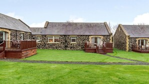 A stone building with a grassy lawn and wooden deck. - 3 Bed in Alnwick (oc-80479) (Newton-by-the-Sea)