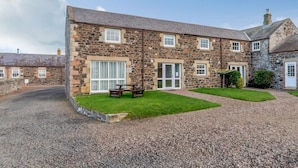 A stone building with a gravel driveway, a grassy lawn, and a picnic table. - 4 Bed in Alnwick (oc-80484) (Newton-by-the-Sea)