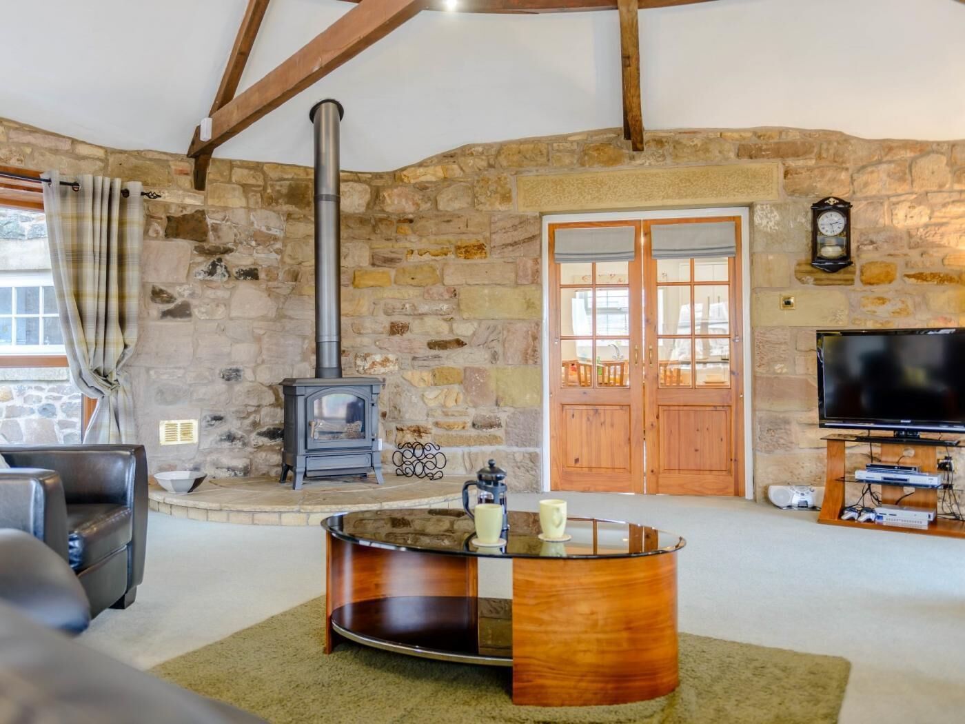 Un intérieur rustique avec un mur en pierre, un poêle à bois, une porte en bois, un téléviseur et une table basse en verre.