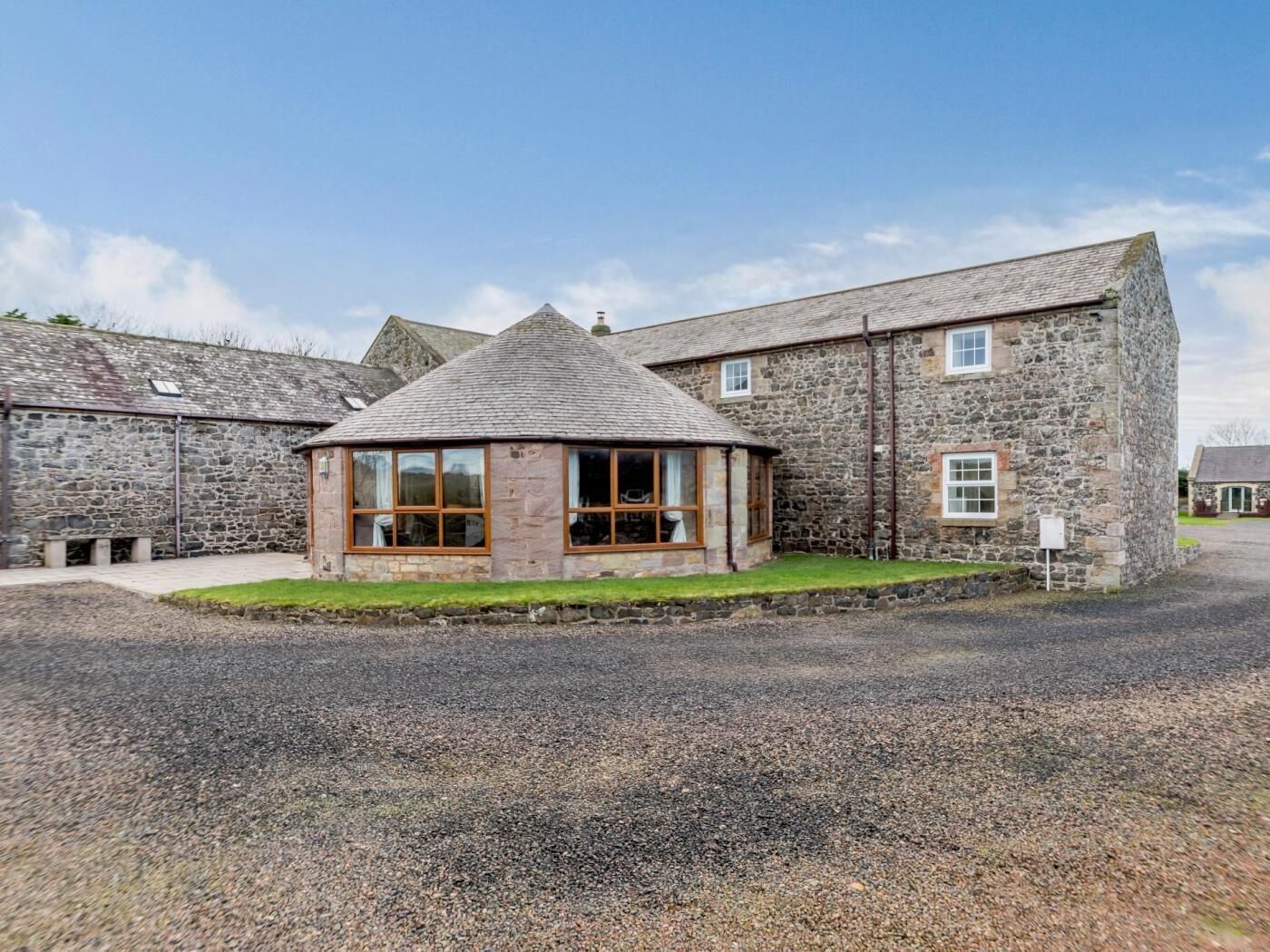 A stone building with a central glass room and a gravel driveway.