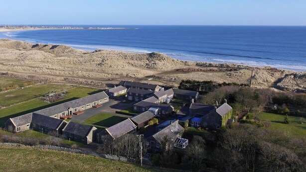 A coastal residential area with stone houses, a clear view of the sea, and a grassy field. - 4 Bed in Alnwick (oc-80484) (Newton-by-the-Sea)