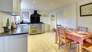 A kitchen with a central island, a dining table with a red and white checkered tablecloth, and a black range hood above the stove. - 2 Bed in Orford (oc-sflis) (Orford)